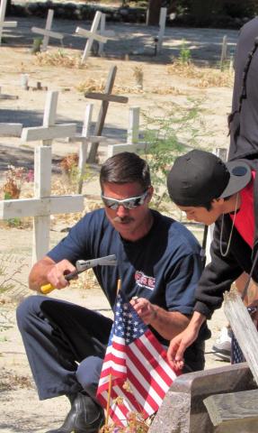 Soboba Fire Department Captain Raul Licon and Soboba Youth Council member Jesse Garcia place a flag on the gravesite of a veteran at Soboba Cemetery on May 21