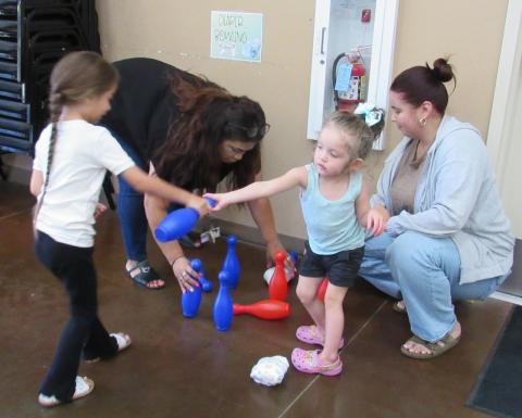 Two-year-old Millie Razon, right, helps pre-k teachers Ana Garcia and Alaina Adkins with the bowling game by handing a pin to Avelaka Leal Two-year-old Millie Razon, right, helps pre-k teachers Ana Garcia and Alaina Adkins with the bowling game by handing a pin to Avelaka Leal