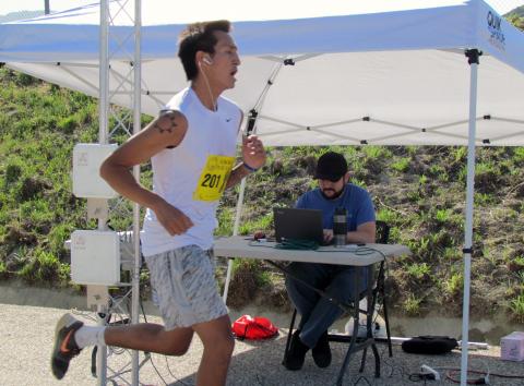 Male division 5K winner, Kina Brings-Plenty from Riverside, crosses the finish line as Chad Timmermans of Negative Split Running clocks him on the computer Male division 5K winner, Kina Brings-Plenty from Riverside, crosses the finish line as Chad Timmermans of Negative Split Running clocks him on the computer